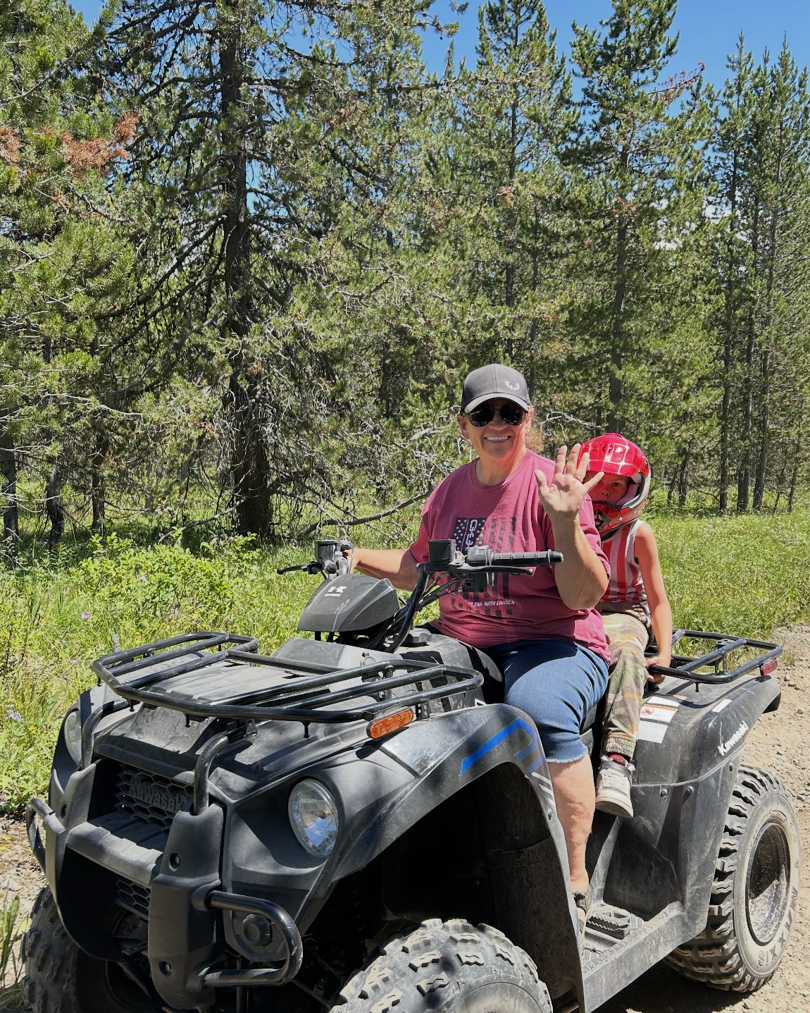 Julie Knight riding a four-wheeler on a forest trail in the Idaho mountains with one of her grandchildren