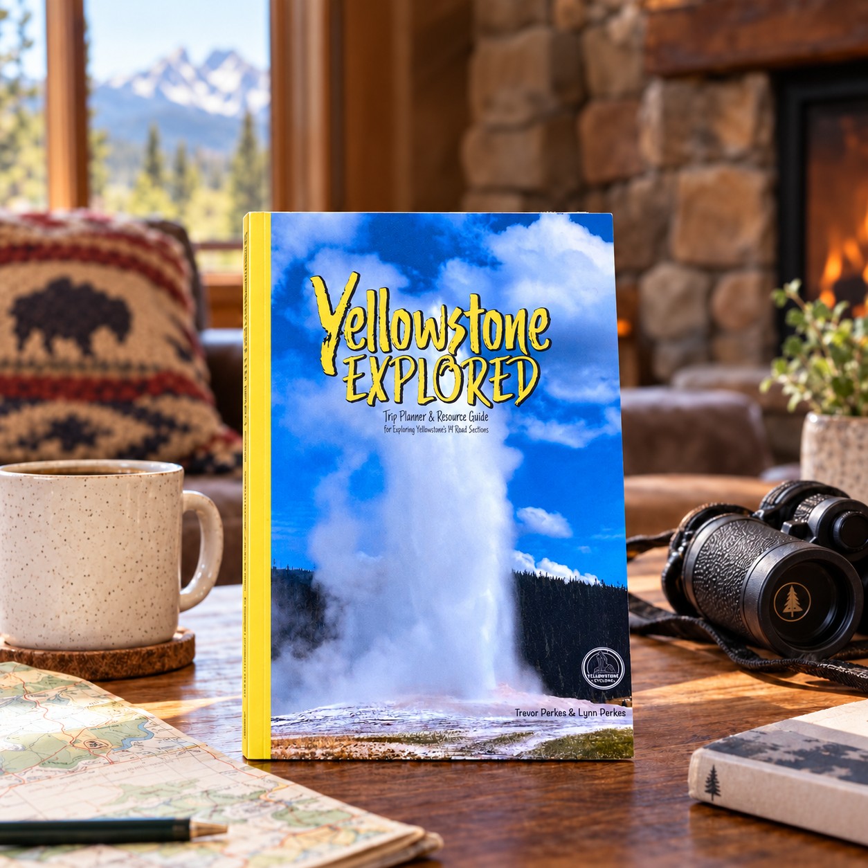 Yellowstone Explored, the trip planner and resource guide, standing on a table beside a park map, a mug and binoculars